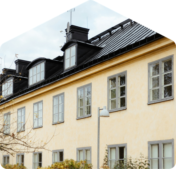 Gult tvåvåningshus med svart plåttak, välvda takkupor och sexdelade fönster, med lyktstolpe och höstkvistar i förgrunden